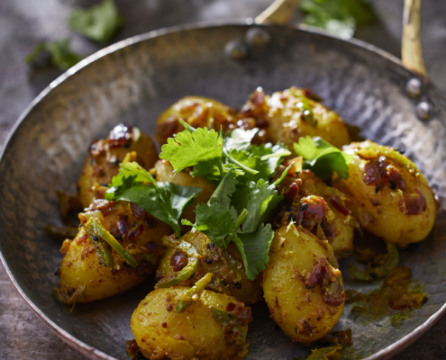 Detailaufnahme gebratener Currykartoffeln mit Koriander und aromatischen Gewürzen.