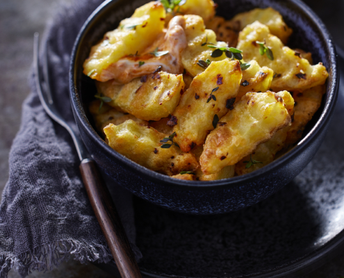 Detailaufnahme knuspriger Mini-Ofen-Pommes mit Kräutern und Dip.